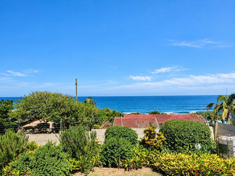 A scenic elevated view overlooking the ocean, featuring lush garden landscaping and a secure boundary wall with electric fencing.