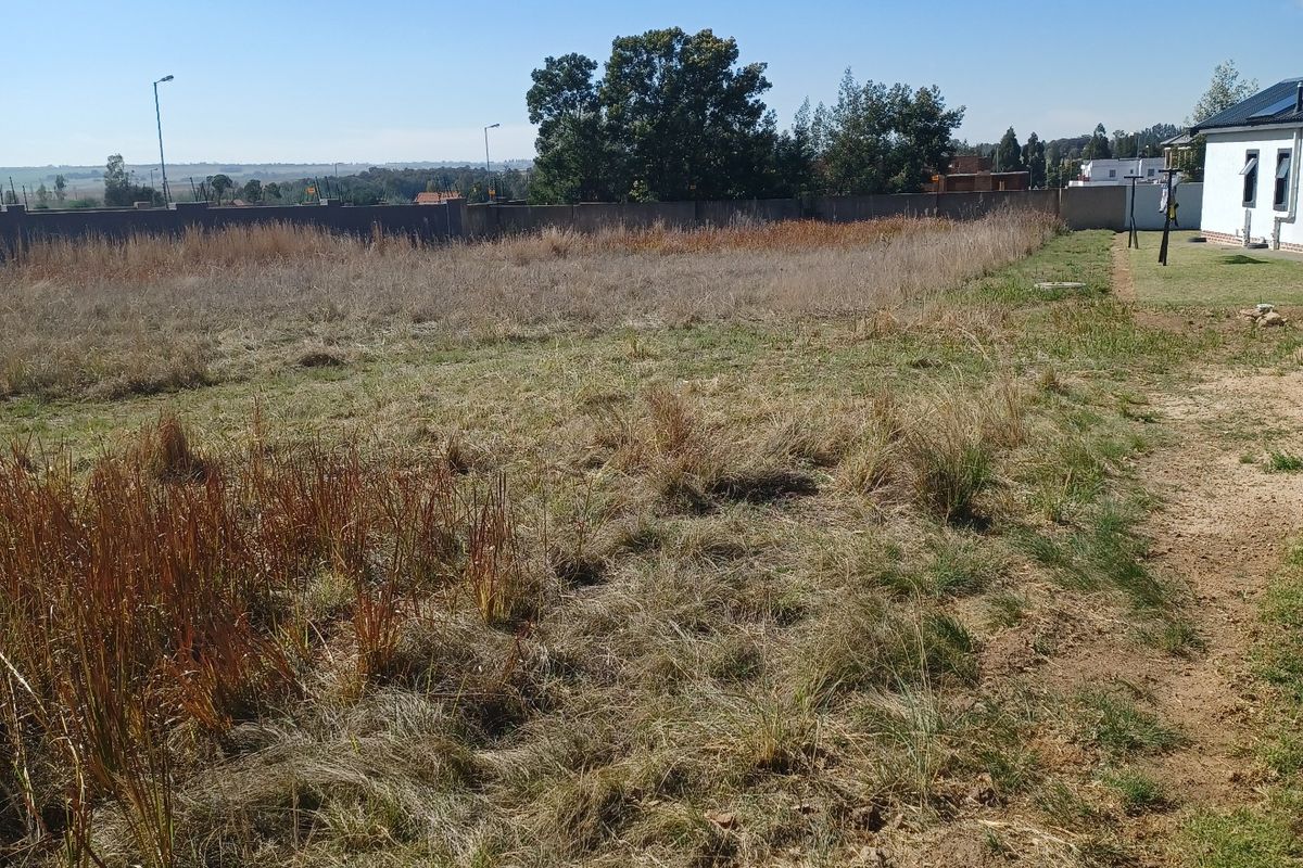 A vacant residential plot featuring natural grass coverage, perimeter walling, and clear views of the surrounding landscape.