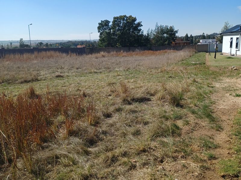 A vacant residential plot featuring natural grass coverage, perimeter walling, and clear views of the surrounding landscape.