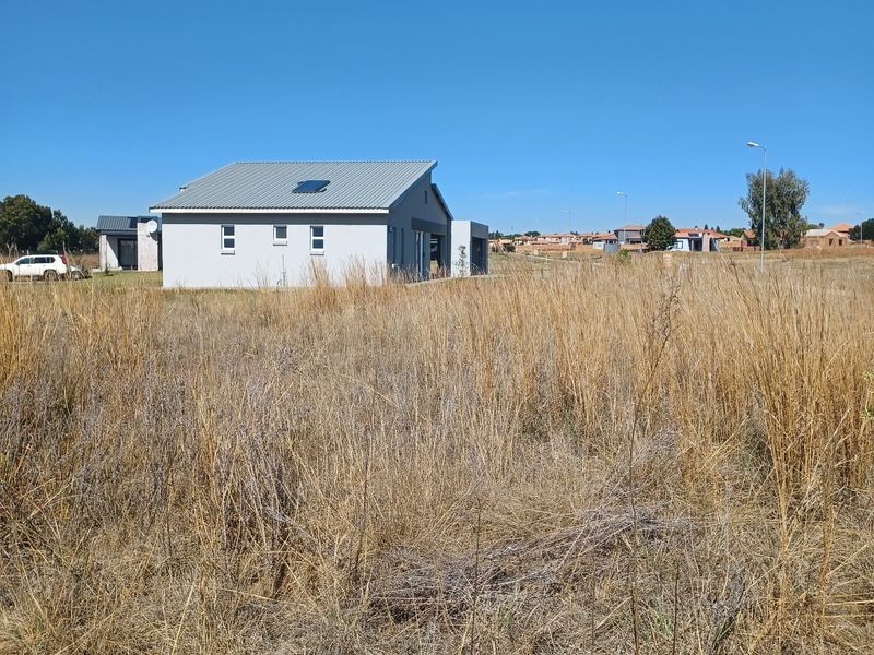 A view of a modern residential property situated on a large, undeveloped plot of land with dry grass.
