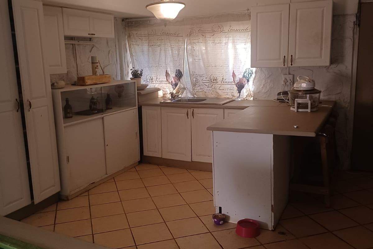 A dated kitchen featuring white built-in cabinetry, laminate countertops, and tiled flooring, offering significant potential for a modern renovation and layout update.