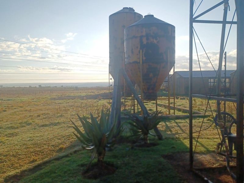 Outdoor farm area featuring two large metal grain silos and a windmill tower structure set against a rural landscape.