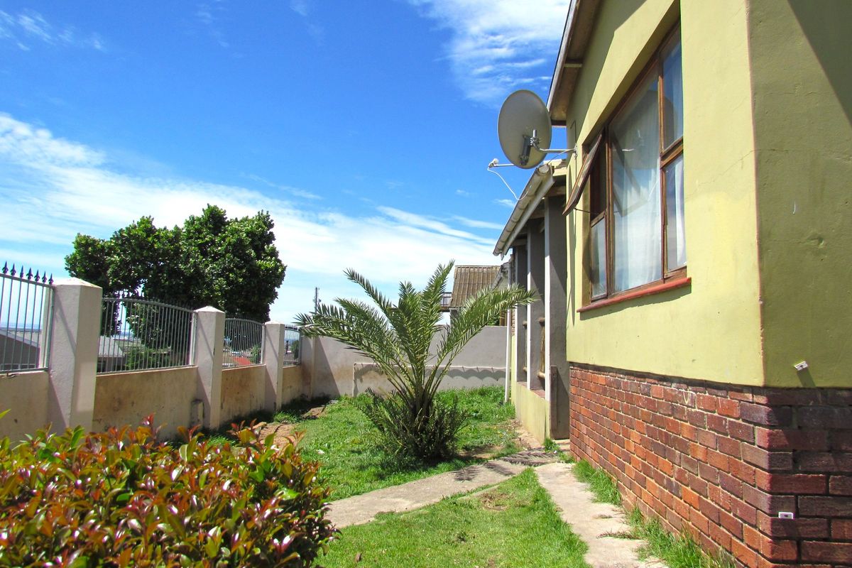 Rear exterior view of the property featuring a brick and painted facade, perimeter fencing, and a small garden area with a concrete pathway.
