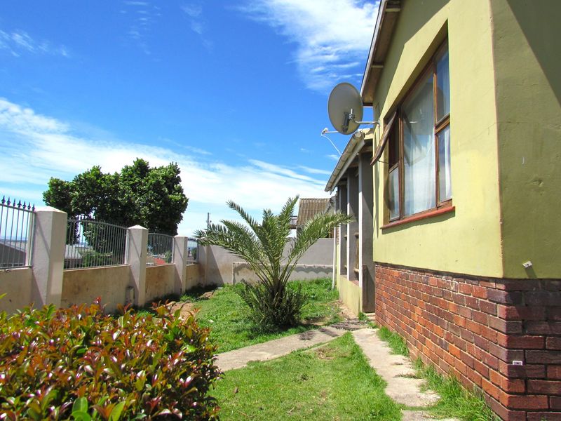 Rear exterior view of the property featuring a brick and painted facade, perimeter fencing, and a small garden area with a concrete pathway.