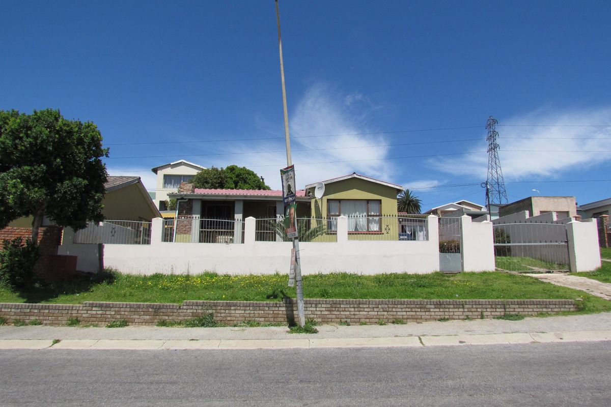 Front view of a residential property featuring a perimeter wall, metal gate, and brick retaining wall along the street frontage.