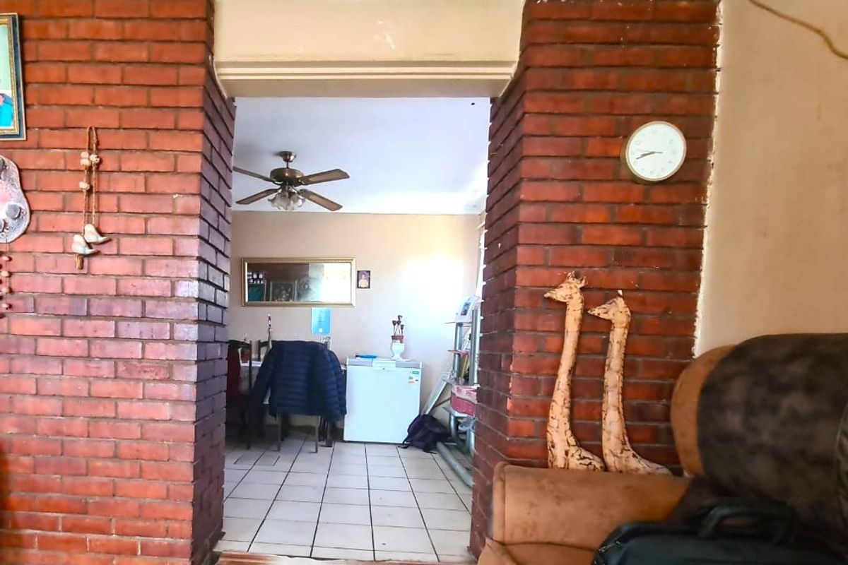 Living area featuring a distinctive exposed brick archway leading to an adjacent space with tiled flooring and a ceiling fan.