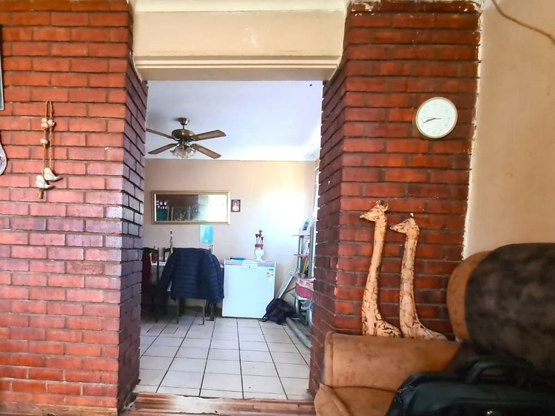 Living area featuring a distinctive exposed brick archway leading to an adjacent space with tiled flooring and a ceiling fan.