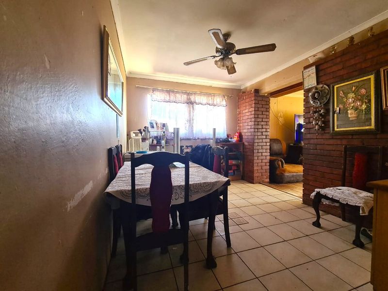 Dining area featuring tiled flooring, a ceiling fan, and an exposed brick feature pillar, requiring cosmetic updates to the wall finishes.