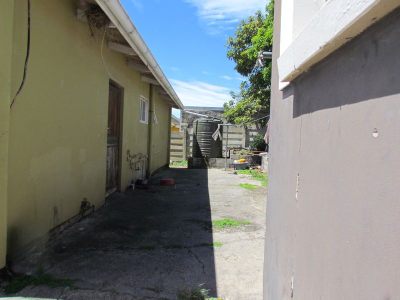 A view of the rear exterior area featuring concrete paving, a water tank, and boundary walling, showing signs of wear and maintenance requirements.
