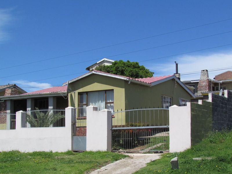 Front exterior view of a single-story house featuring a metal perimeter fence, gated driveway, and a corrugated metal roof.