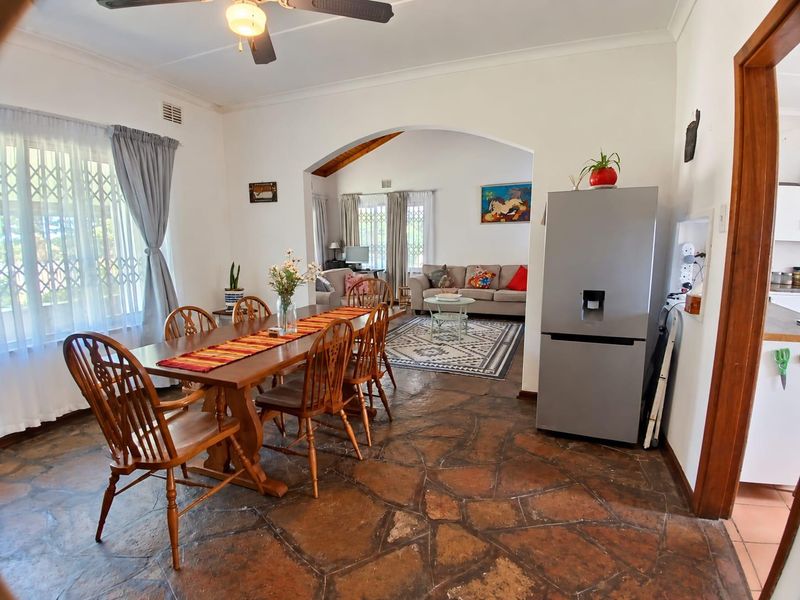 Open plan dining and living area featuring rustic stone flooring, a ceiling fan, and a wide archway connecting the two living spaces.