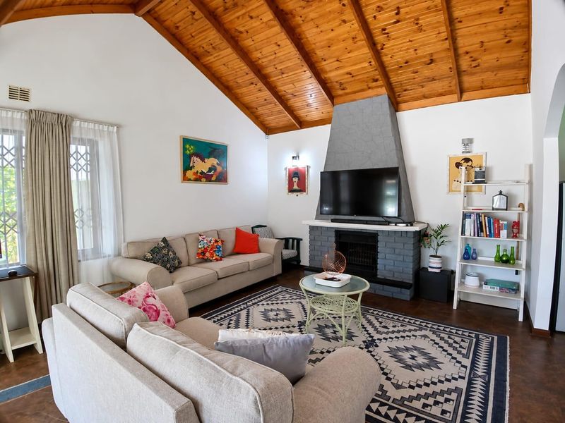 Spacious living room featuring a high vaulted timber ceiling with exposed beams and a prominent stone-clad fireplace as a central focal point.