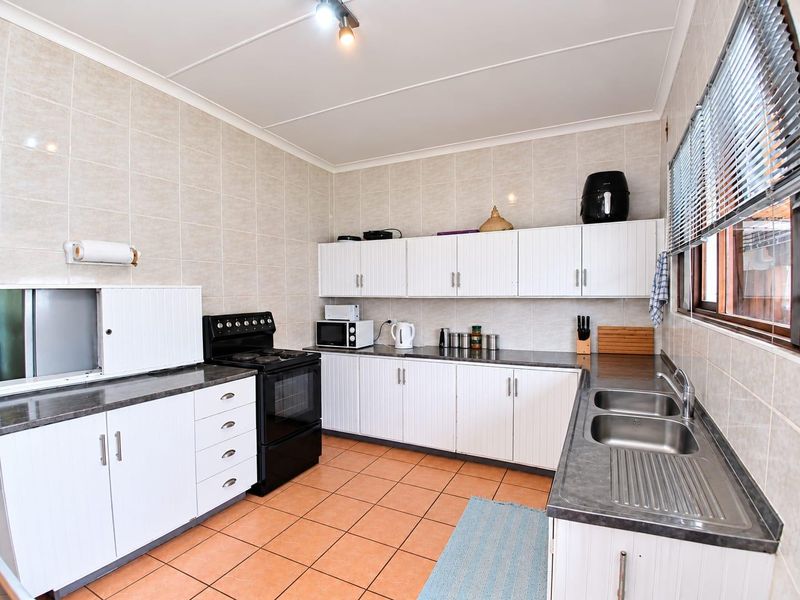 A functional kitchen featuring white cabinetry, laminate countertops, a double stainless steel sink, and a freestanding stove with tiled splashbacks and flooring.