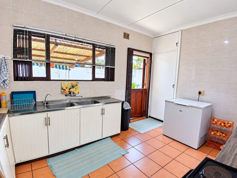 Functional kitchen featuring tiled flooring, stainless steel double sink, ample cabinetry, and direct access to the exterior.