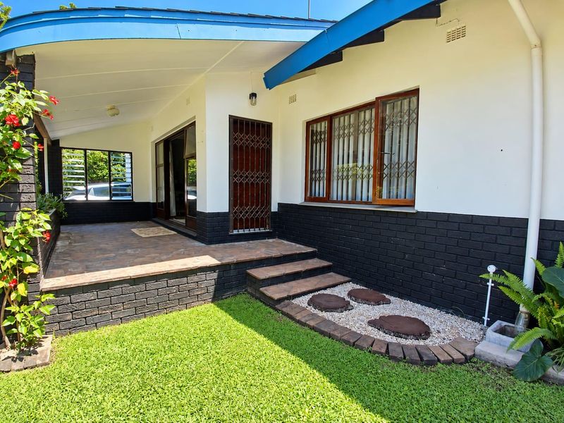 A well-maintained covered patio area featuring stone tiling, brick accents, and direct access to a landscaped garden with stepped entry.