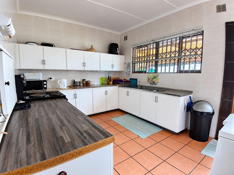 Functional kitchen featuring white cabinetry, dark laminate countertops, ceramic tile flooring, and a large window with security bars for natural light.