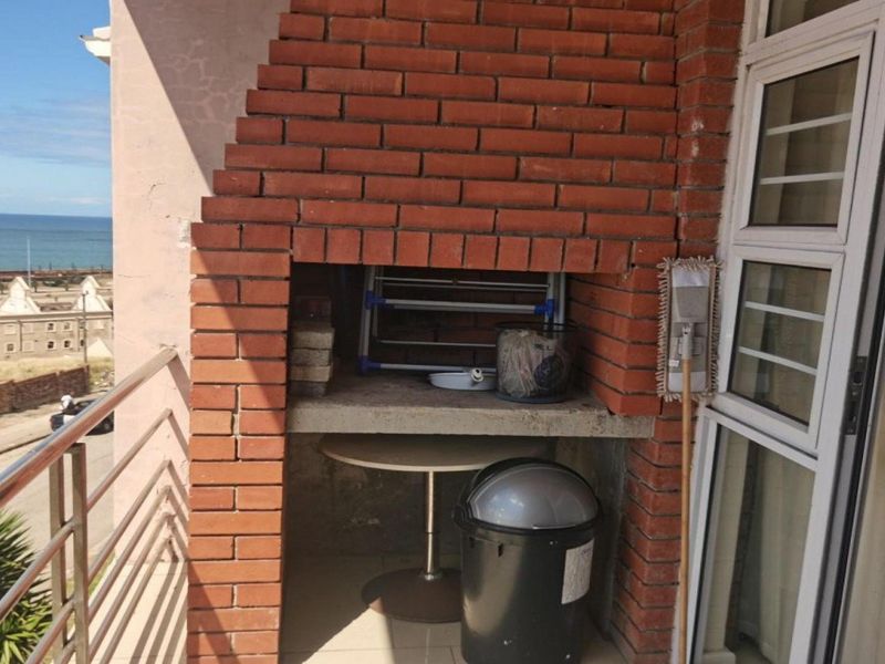 A balcony featuring a built-in brick braai area with a concrete countertop, offering an outdoor space with coastal views.