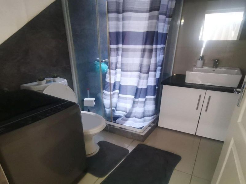 A functional bathroom featuring a shower enclosure, a modern vessel sink with a vanity cabinet, and tiled finishes throughout.