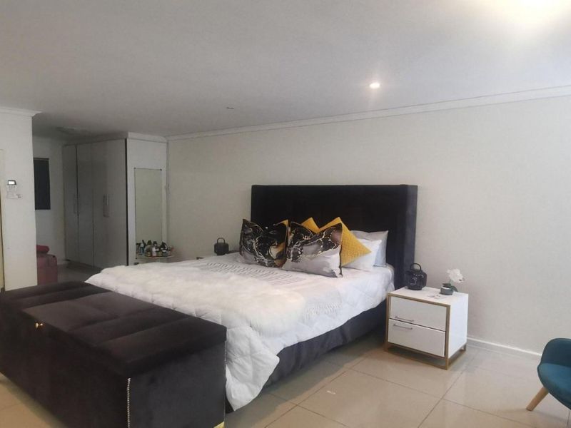 Spacious bedroom featuring neutral tiled flooring, recessed downlighting, and integrated built-in cupboards for ample storage.