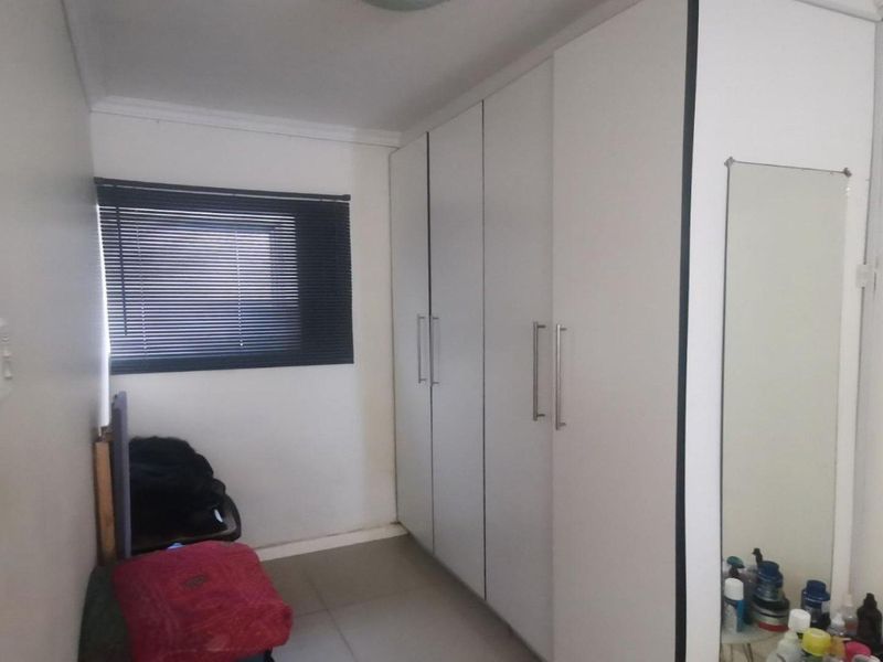 A functional bedroom featuring white built-in cupboards, tiled flooring, and a window fitted with dark venetian blinds.