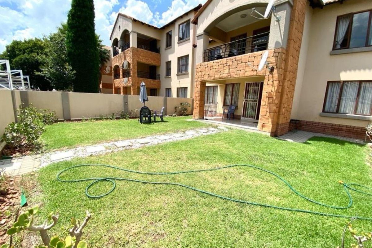 Rear view of a townhouse featuring a private garden, stone-clad facade, and a covered patio area with wrought iron railings.