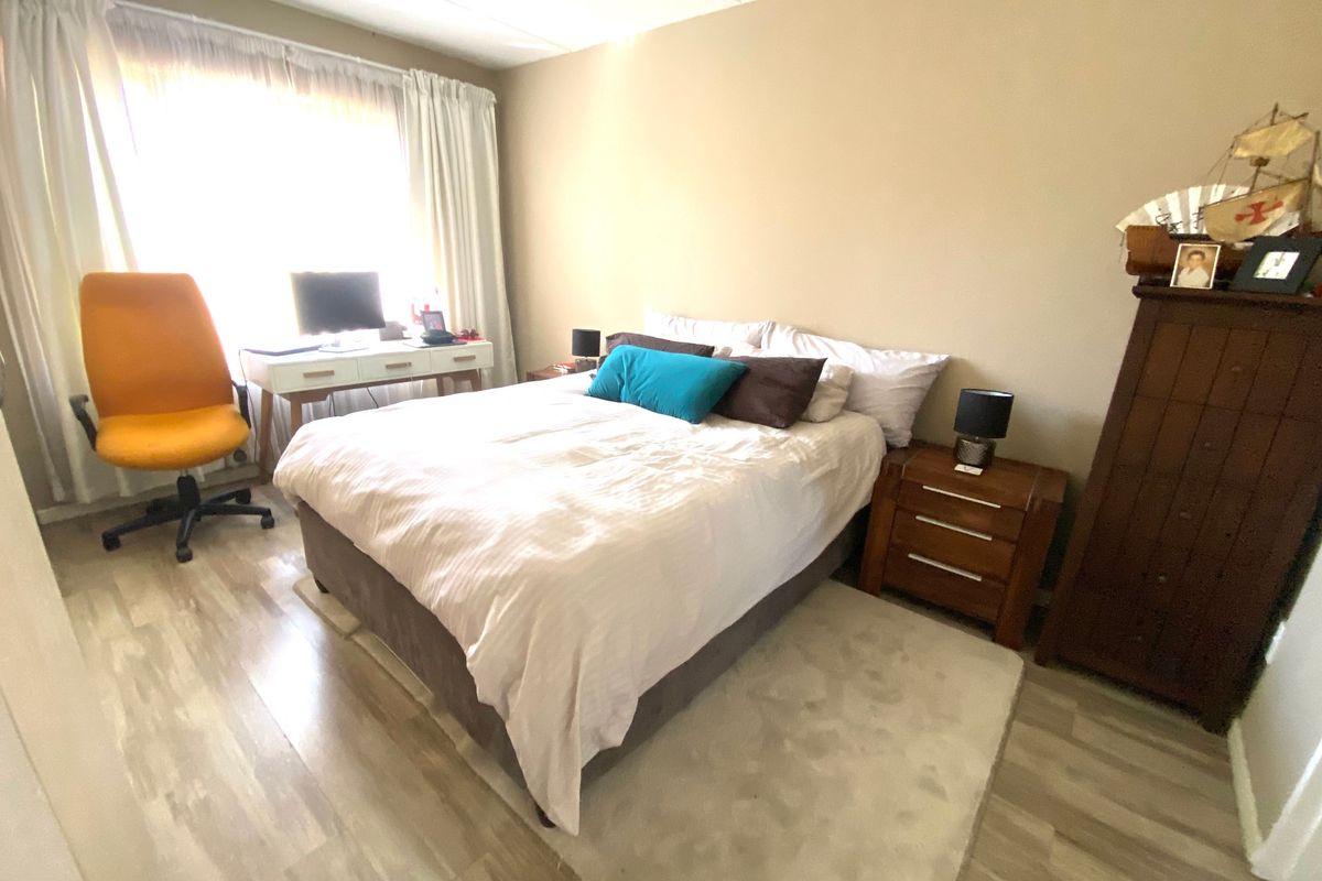 A functional bedroom featuring light-toned laminate flooring and a large window with curtain tracks, providing a neutral base for personalization.