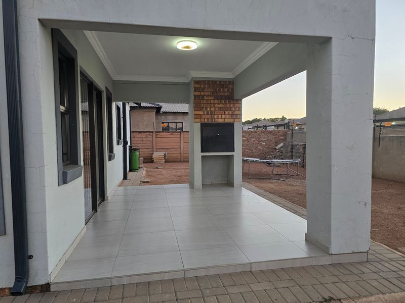Covered patio area featuring tiled flooring and a built-in braai, providing a functional outdoor entertainment space overlooking the rear garden.