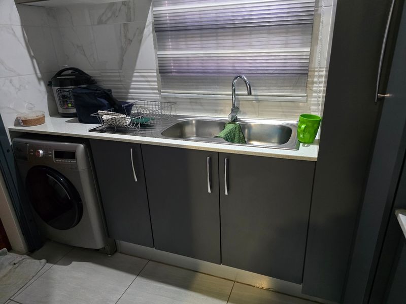 A functional laundry area featuring a double stainless steel sink, stone countertop, modern cabinetry, and tiled splashback.