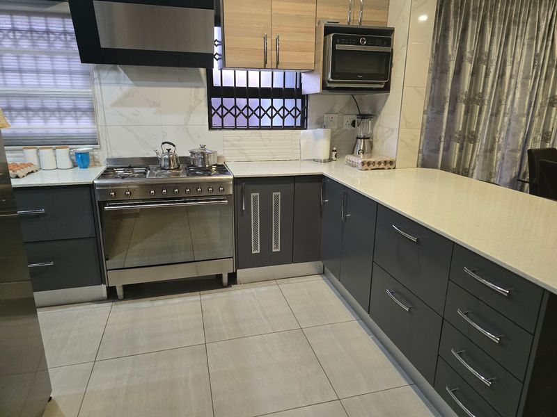 Modern kitchen featuring dark grey cabinetry, light quartz countertops, gas stove with extractor fan, and built-in microwave, complemented by neutral tiled flooring.