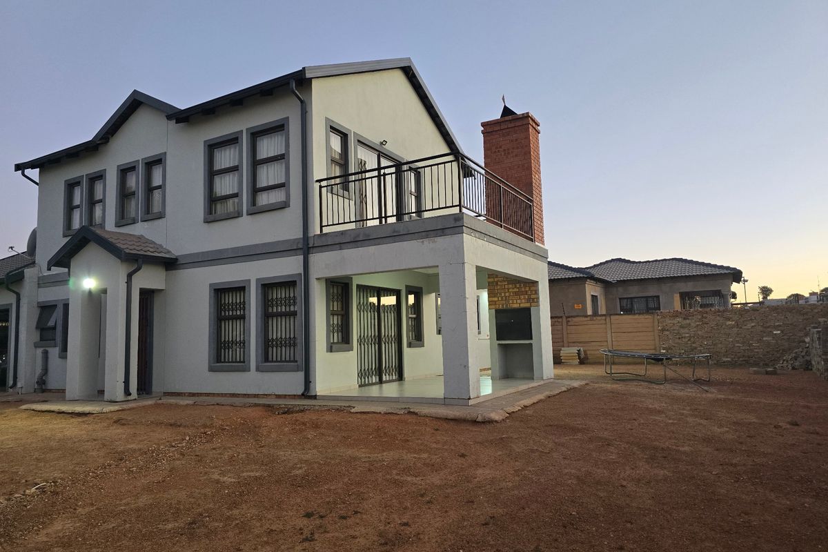 Rear view of a double-story house featuring a balcony, built-in braai area, and a spacious backyard with potential for landscaping.