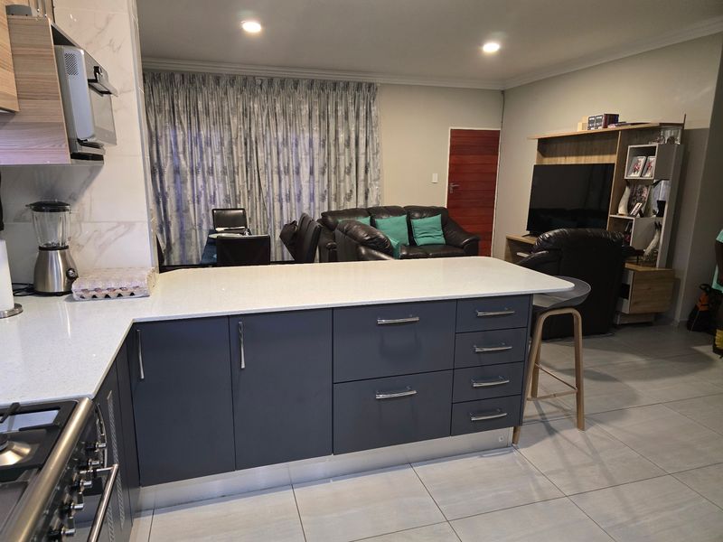 Modern open-plan living area featuring a contemporary kitchen with a central island, quartz countertops, and sleek cabinetry, seamlessly flowing into the lounge space.