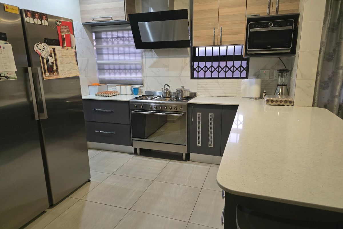 Modern kitchen featuring quartz countertops, built-in cabinetry, a gas stove with extractor fan, and integrated microwave, finished with neutral floor tiles.