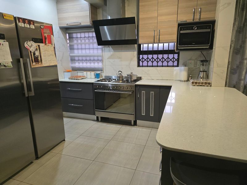 Modern kitchen featuring quartz countertops, built-in cabinetry, a gas stove with extractor fan, and integrated microwave, finished with neutral floor tiles.