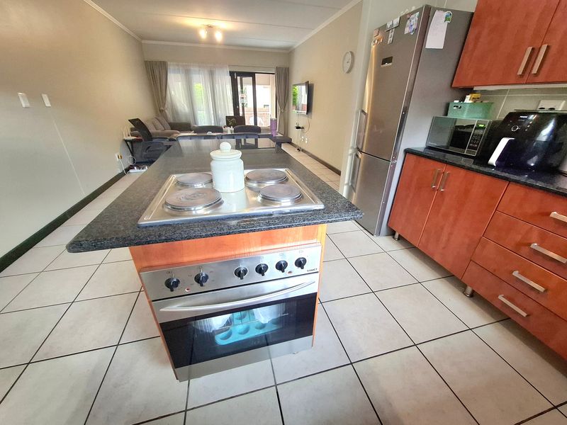 Open-plan living area featuring a central kitchen island with built-in oven and hob, flowing into a lounge space with access to a patio.