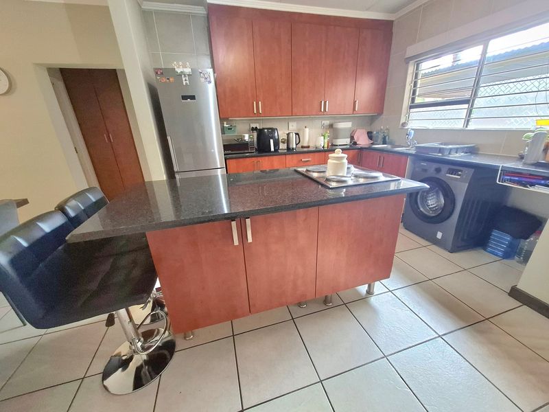 A functional kitchen featuring wooden cabinetry, granite countertops, a central island with an integrated hob, and tiled flooring.