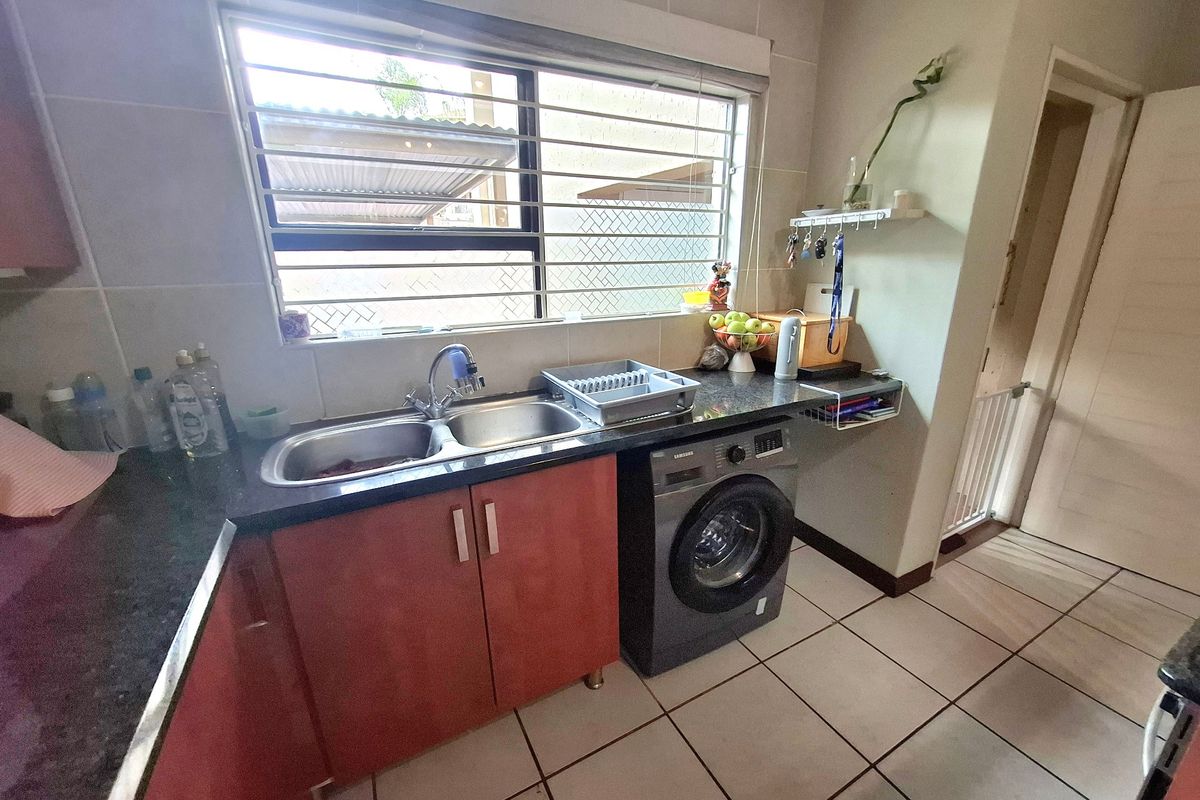 A functional kitchen area featuring granite countertops, double stainless steel sink, built-in cabinetry, and an integrated washing machine under the counter.
