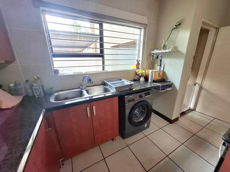 A functional kitchen area featuring granite countertops, double stainless steel sink, built-in cabinetry, and an integrated washing machine under the counter.