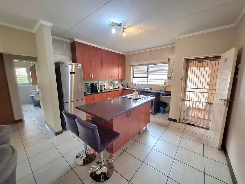 A functional kitchen featuring wooden cabinetry, a central island with a breakfast bar, tiled flooring, and direct access to an outdoor area via a security gate.
