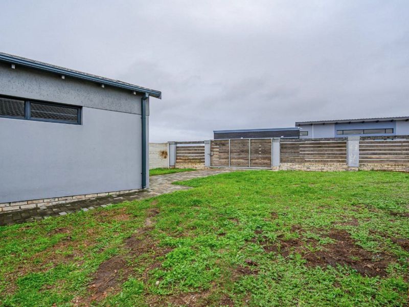 A rear garden area featuring a paved walkway, timber slat fencing, and a metal gate, providing a private outdoor space.