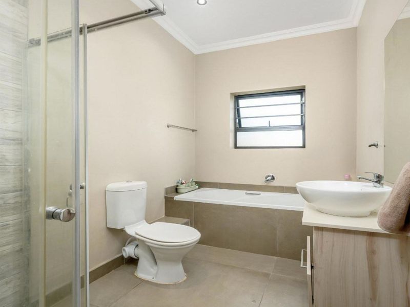 A well-maintained bathroom featuring a glass-enclosed shower, a built-in bathtub, a modern vessel sink on a vanity cabinet, and neutral tiled finishes.