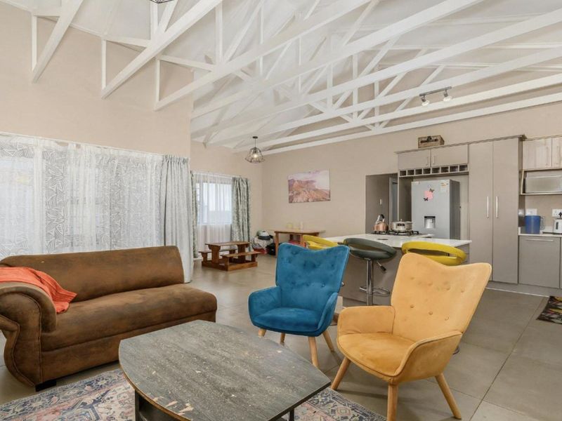 Spacious open-plan living area featuring high vaulted ceilings with exposed white trusses, integrated kitchen cabinetry, and a central island, creating a bright, airy atmosphere.