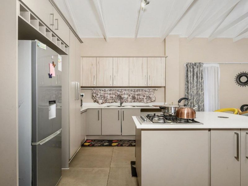 Modern kitchen featuring built-in cabinetry, a central island with a gas hob, double sink, and distinctive exposed beam ceilings.
