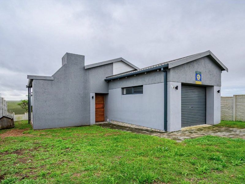 Front elevation of a modern grey-rendered house featuring a single roller garage door, timber entrance door, and a paved driveway set within a fenced yard.