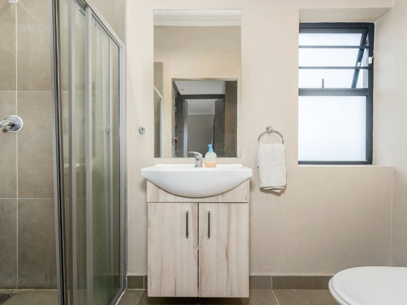 A clean and functional bathroom featuring a glass-enclosed shower, a modern vanity with basin, and a louvered window for natural ventilation.