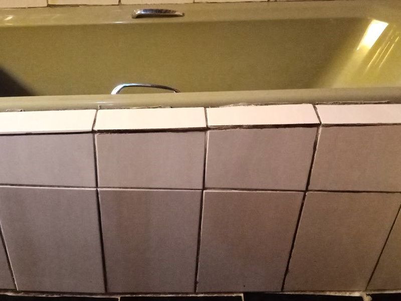 A bathroom featuring a built-in bathtub with tiled surround, showing signs of wear and dated finishes.