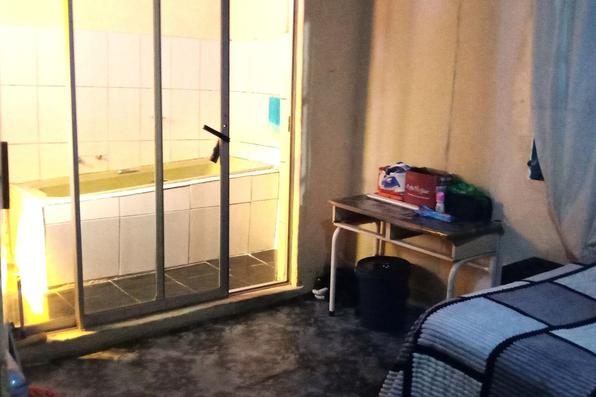 A bedroom featuring an en-suite bathroom area separated by a sliding glass door, including a built-in bathtub with tiled surround.