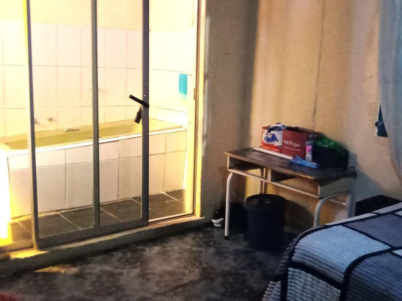 A bedroom featuring an en-suite bathroom area separated by a sliding glass door, including a built-in bathtub with tiled surround.
