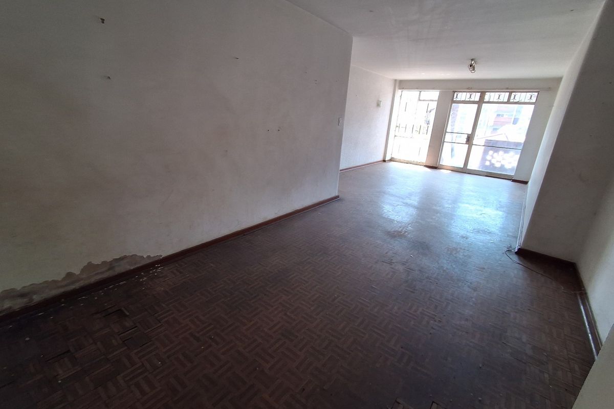 An empty living room featuring original parquet flooring and large sliding glass doors, requiring cosmetic renovation and floor repairs.