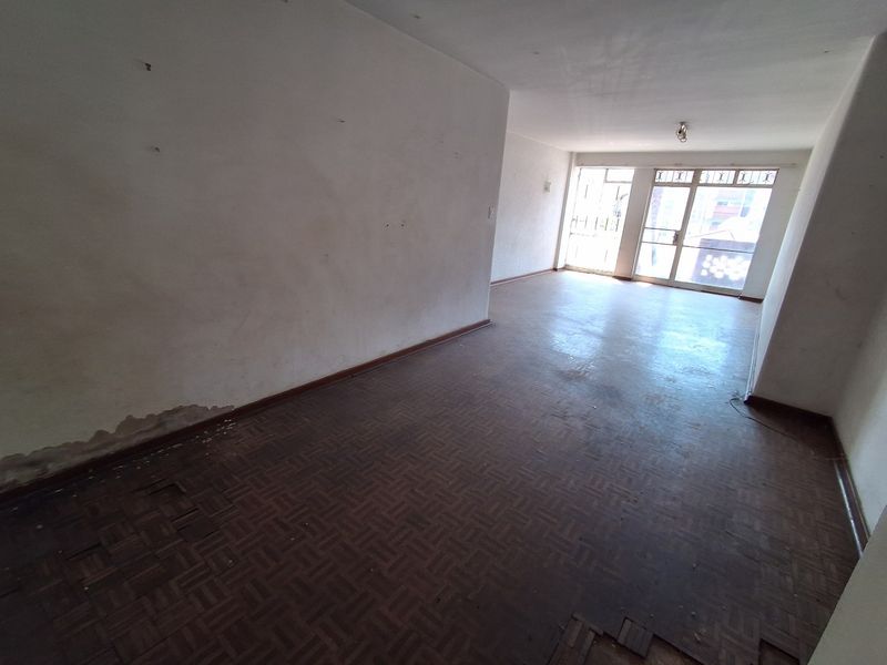 An empty living room featuring original parquet flooring and large sliding glass doors, requiring cosmetic renovation and floor repairs.