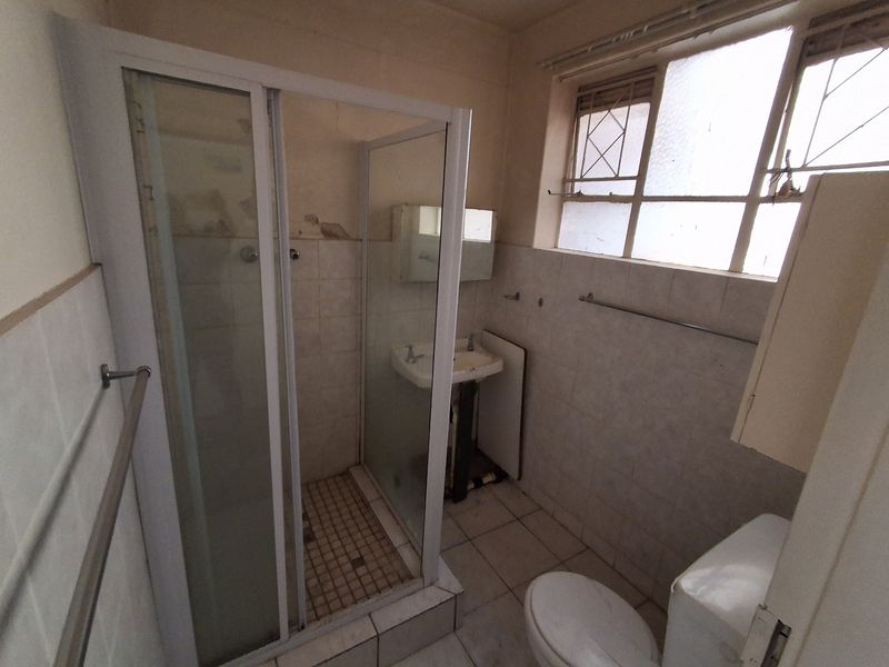 A dated bathroom featuring a shower enclosure, pedestal basin, and toilet, requiring renovation to update the worn finishes and wall surfaces.